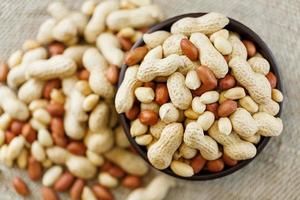 Peanuts in the shell and peeled close-up in cups. Roasted peanuts in their shells and peeled against a brown cloth. photo