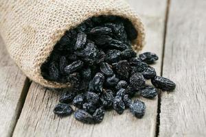 Black raisins in burlap bag over wooden gray table photo
