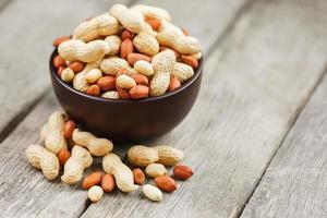 Roasted peanuts in the shell and peeled in a cup, against a gray wooden table photo