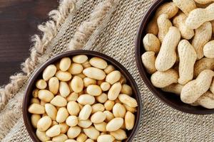 Peanuts in the shell and peeled close-up in cups. Roasted peanuts in their shells and peeled against a brown cloth. photo