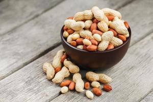 Roasted peanuts in the shell and peeled in a cup, against a gray wooden table photo