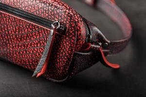 riñonera confeccionada en piel texturizada con manchas en negro y rojo sobre un fondo oscuro de piedra. elegante bolso negro y rojo con cremallera. cuero genuino, hecho a mano foto