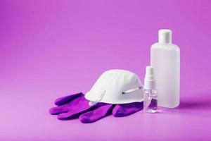 Still life of anti-virus protection on a pink background, mask, rubber gloves, a bottle of hand sanitizer, antiseptic gel. photo