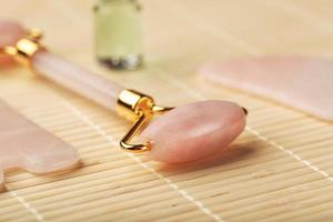 un conjunto de herramientas para la técnica de masaje facial gua sha fabricado en cuarzo rosa natural. rodillo, piedra de jade y aceite en un frasco de vidrio, sobre un fondo de paja para el cuidado de la cara y el cuerpo. foto