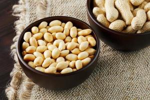 Peanuts in the shell and peeled close-up in cups. Roasted peanuts in their shells and peeled against a brown cloth. photo