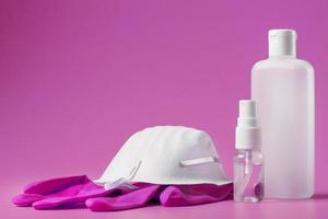Bodegón de protección antivirus sobre fondo rosa, máscara, guantes de goma, una botella de desinfectante para manos, gel antiséptico. foto