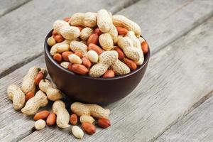 Roasted peanuts in the shell and peeled in a cup, against a gray wooden table photo