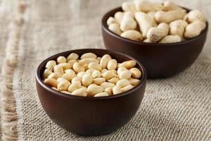 Peanuts in the shell and peeled close-up in cups. Roasted peanuts in their shells and peeled against a brown cloth. photo