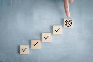 Checklist, Task list, Survey and assessment, Quality Control, Goals achievement and business success. To do list. Hand point to dartboard from top of step of complete with check mark on wooden block. photo