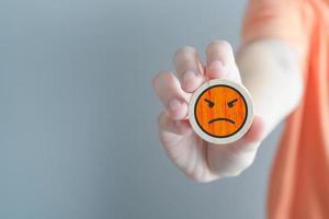 Hand showing angry face on wooden circle. Unhappy, Negative, Mental health assessment, World mental health day, Feedback, Satisfaction, Customer service review concept. photo