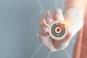 Business achievement goal and objective target. Growing business success concept. Hand showing wood block with dart board icon and arrow pointing to the target. photo