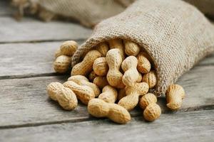 Peanuts in a miniature burlap bag on old, gray wooden surface photo