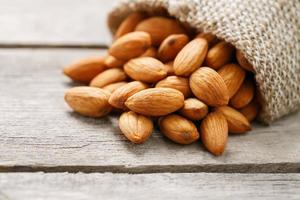 Almond nuts in a burlap bag on a wooden gray background. photo