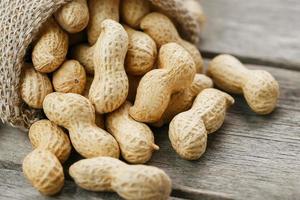 Peanuts in a miniature burlap bag on old, gray wooden surface photo