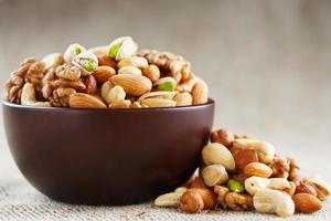 Mix of different nuts in a wooden cup against the background of fabric from burlap. Nuts as structure and background, macro. Top view. photo