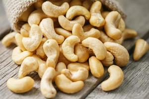 Cashew nuts in burlap bag on wooden gray background . Healthy food photo