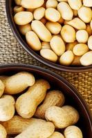 Peanuts in the shell and peeled close-up in cups. Roasted peanuts in their shells and peeled against a brown cloth. photo