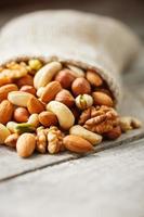 Mix of different nuts in a wooden cup against the background of fabric from burlap. Nuts as structure and background, macro. Top view. photo