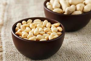 Peanuts in the shell and peeled close-up in cups. Roasted peanuts in their shells and peeled against a brown cloth. photo