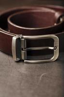 Fashionable men's brown belt made of genuine leather with a light metal buckle on a dark background. Genuine leather, handmade photo