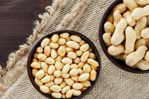 Peanuts in the shell and peeled close-up in cups. Roasted peanuts in their shells and peeled against a brown cloth. photo