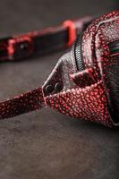 Belt bag made of textured, spotty black and red leather on a stone dark background. Elegant black and red bag with a zipper. Genuine leather, handmade photo