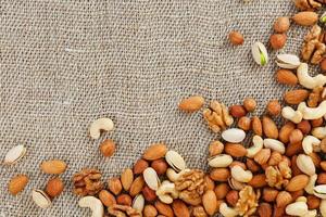 Mix of different nuts in a wooden cup against the background of fabric from burlap. Nuts as structure and background, macro. Top view. photo