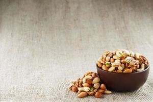 Mix of different nuts in a wooden cup against the background of fabric from burlap. Nuts as structure and background, macro. Top view. photo