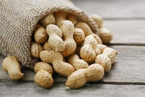 Peanuts in a miniature burlap bag on old, gray wooden surface photo