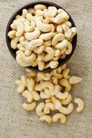 Cashew nuts in a wooden bowl on a burlap cloth background. photo