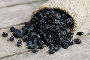 Black raisins in burlap bag over wooden gray table photo