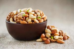 Mix of different nuts in a wooden cup against the background of fabric from burlap. Nuts as structure and background, macro. Top view. photo