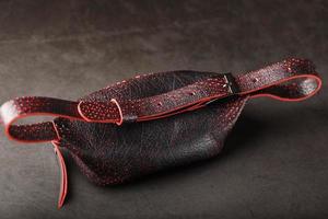 Belt bag made of textured, spotty black and red leather on a stone dark background. Elegant black and red bag with a zipper. Genuine leather, handmade photo