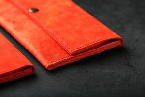 A pair of red genuine leather wallets with rivets on a dark background top view. Genuine leather photo