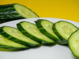 A smooth, medium-sized cucumber on white plate, sliced. Cucumber on a yellow background. photo