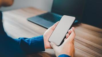 Mockup image of a man holding and using smartphone with blank desktop screen while working and drinking coffee in cafe. photo