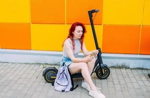 Woman uses a smartphone and an electric scooter in the summer in the city photo