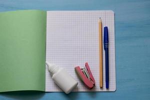 School supplies on a notebook sheet. School concept with stationery. School notebook, glue, stapler, pencil and pen. Schoolchild and student studies accessories. photo