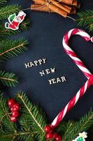 árbol de navidad con adornos y dulces sobre un fondo negro. la inscripción feliz año nuevo foto