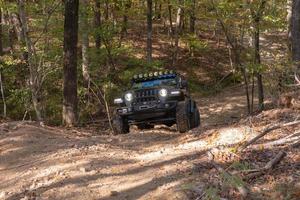 Hot Springs, AR, USA, 2022 - A frontal view of a black Jeep Rubicon scaling a hillside on a forest trail. photo