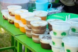 Puddings in plastic containers are placed on a green table, sold by street vendors photo