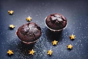 Sweet chocolate muffins surrounded by golden stars on a black background covered with white dust photo