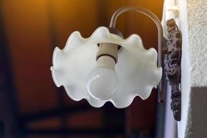 Wall lamp, designed in a round white plate with serrated edges, mounted on the wall of the patio, balcony to provide illumination at night. Soft and selective focus. photo