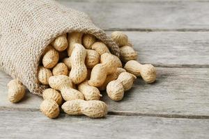 Peanuts in a miniature burlap bag on old, gray wooden surface photo