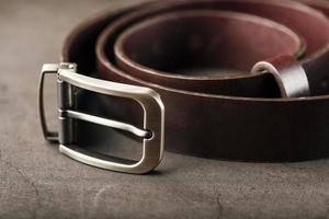 cinturón marrón de moda para hombres hecho de cuero genuino con una hebilla de metal claro sobre un fondo oscuro. cuero genuino, hecho a mano