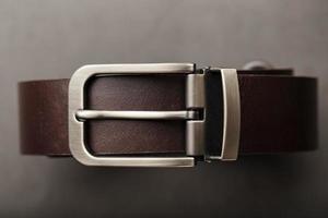 cinturón marrón de moda para hombres hecho de cuero genuino con una hebilla de metal claro sobre un fondo oscuro. cuero genuino, hecho a mano
