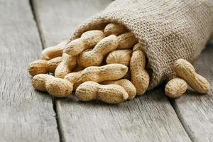 Peanuts in a miniature burlap bag on old, gray wooden surface photo