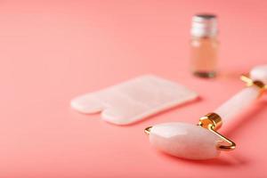 A set of tools for face Massage technique Gua Sha made of natural rose quartz on a pink background. Roller, jade stone and oil in a glass jar for face and body care. photo