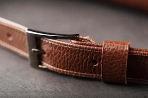 A brown belt bag made of textured brown leather on a black stone background. Elegant fanny pack brown bag with a zipper photo