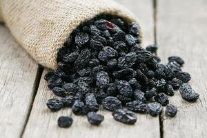 Black raisins in burlap bag over wooden gray table photo